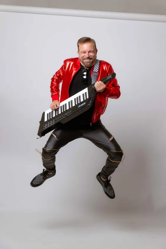 Ray Myers leaping mid-air with a keytar in a red satin jacket